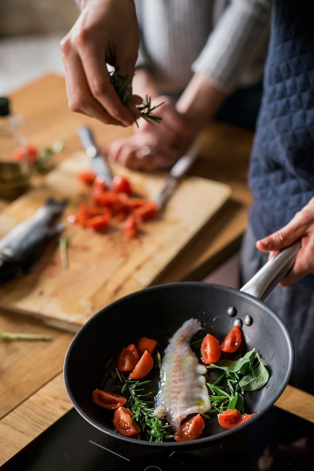 hands of young couple frying fish with herbs at ki